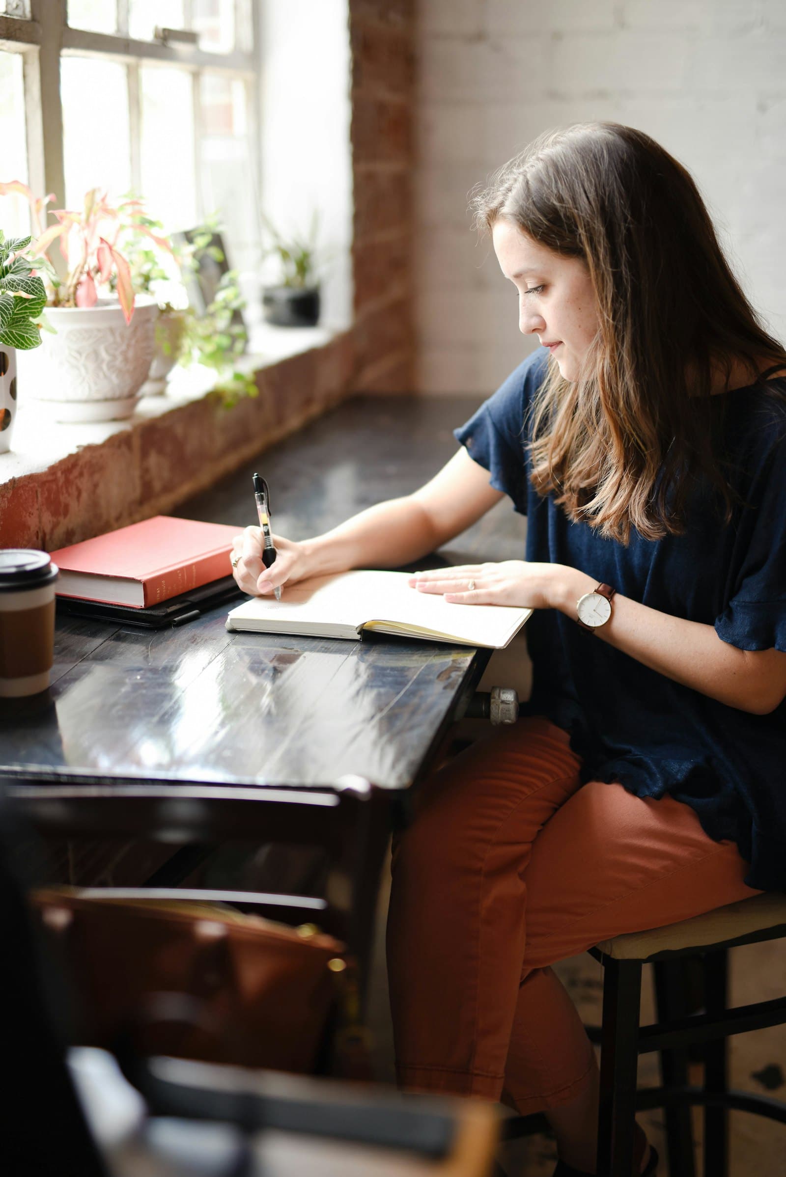 A student writing in a notebook at a table beside a bright window